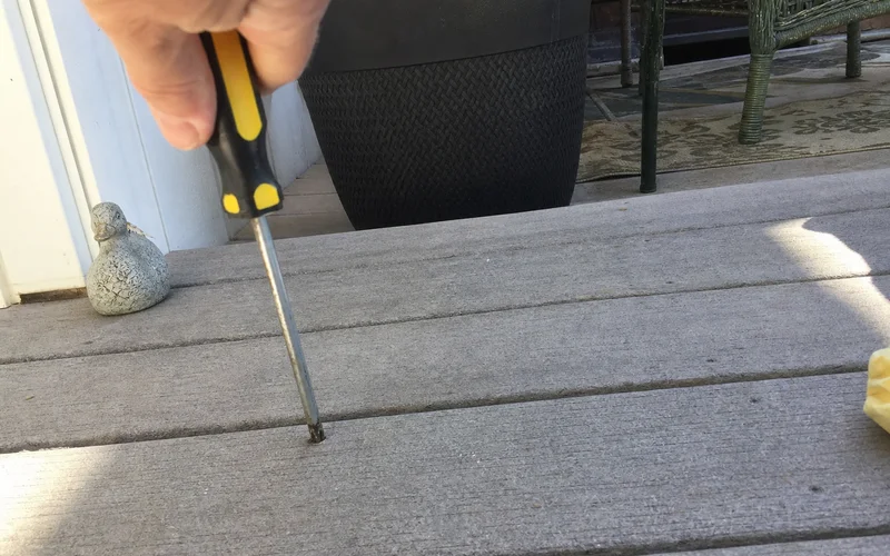 Screwdriver being pushed into a soft deck board to test for wood rot