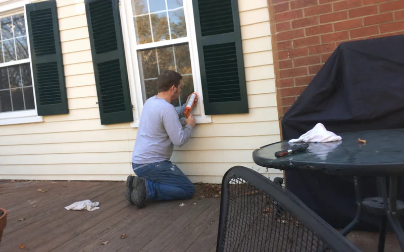 Handyman caulking around window trim before winter