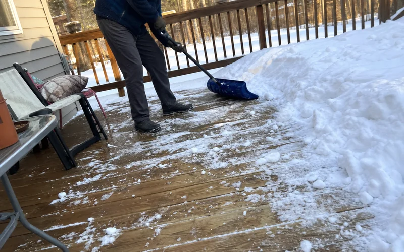 Plastic shovel clearing snow from wood deck